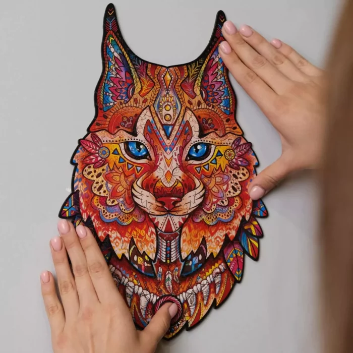 Una maschera colorata e dai motivi intricati Gentle Lynx Unidragon Animali tenuta contro un muro da un paio di mani.