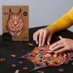 Persona che assembla un puzzle colorato "Gentle Lynx Unidragon Animali" su una superficie scura con la scatola visualizzata sullo sfondo.