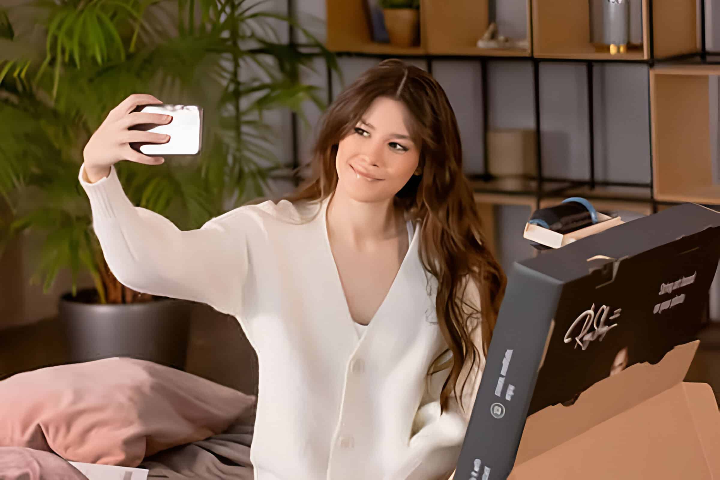 Donna che si scatta un selfie con uno smartphone in un'accogliente stanza illuminata da Ringstring con scatole nelle vicinanze.