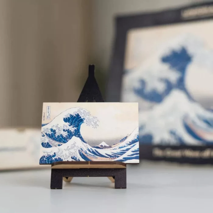 Una replica in miniatura della stampa Unidragon Art "LA GRANDE ONDA AL LARGO DI KANAGAWA" esposta su un supporto in legno con uno sfondo sfocato.