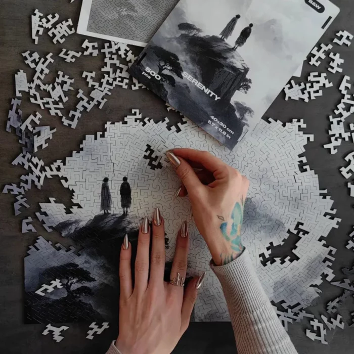 La mano di una persona con un tatuaggio assembla un puzzle su un tavolo, con l'immagine di due figure e un cielo drammatico dal film intitolato "SERENITÀ IN BIANCO E NERO.