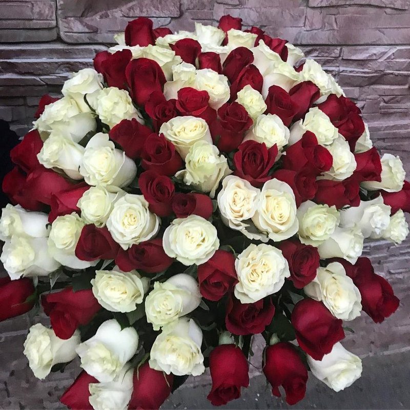 Un grande mazzo di rose rosse e bianche è disposto a forma di cerchio, su uno sfondo con motivo a pietra.
