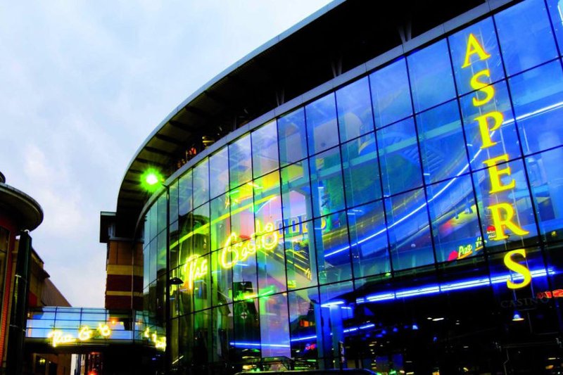 Edificio con facciata in vetro su cui spiccano grandi lettere gialle che compongono la scritta “ASPERS” e luci al neon blu e gialle che si riflettono sulle finestre.